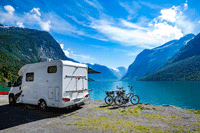 Camper and bikes in front of a scenic lake and mountains