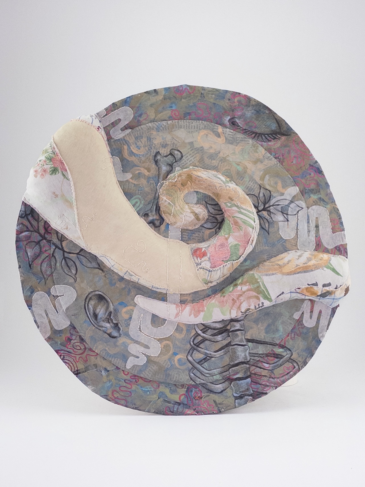 A circular fabric sculpture featuring abstract shapes, and fragmented organic shapes arranged in layers across the art piece.