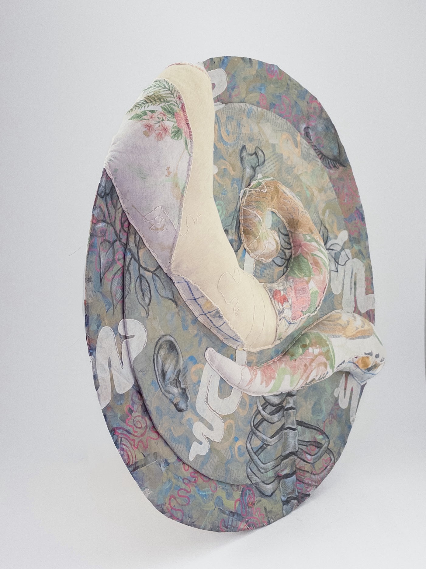 A circular fabric sculpture featuring abstract shapes, and fragmented organic shapes arranged in layers across the art piece.